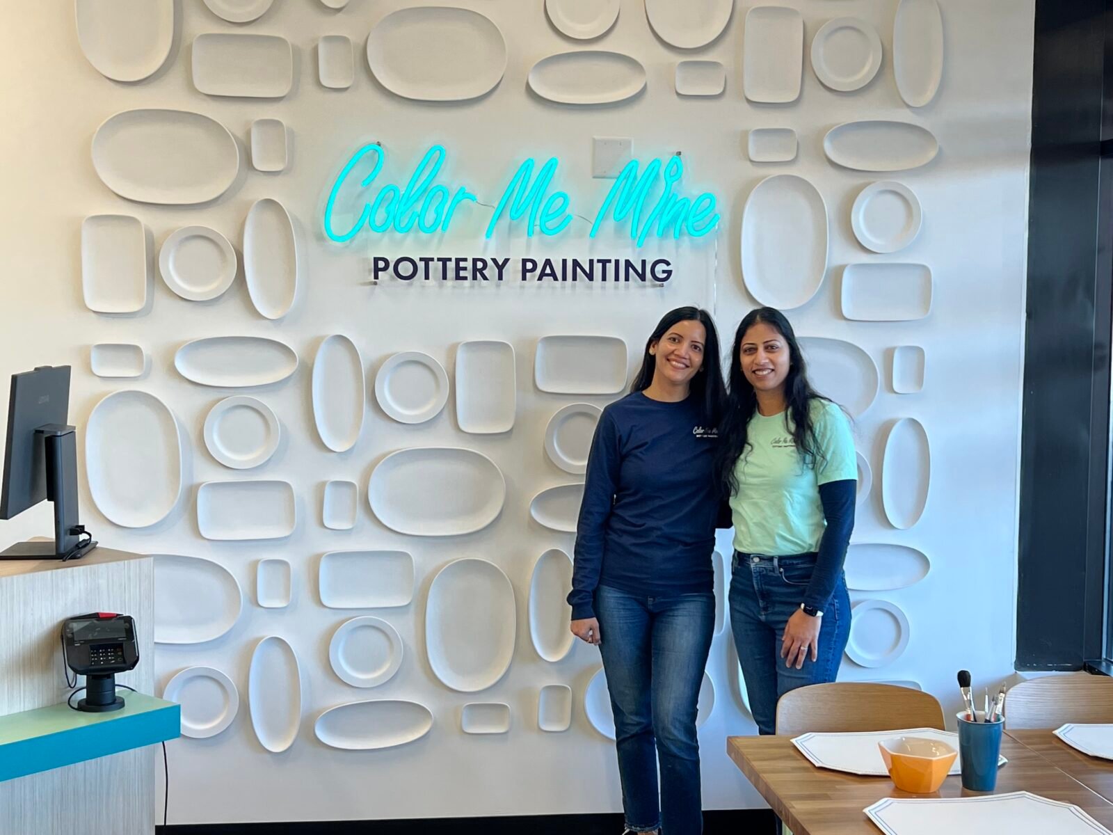 Antima Jain and Pooja Choudhary, co-owners of Color Me Mine Edina, smiling in their vibrant pottery studio.