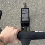 J’ai roulé 500 km avec le Coros Dura 2 Solar et la montée en gamme ne me parait pas toujours justifiée 6 Un cycliste utilisant le compteur GPS Coros Dura 2 Solar sur son vélo, avec un paysage en arrière-plan. L'écran du compteur affiche des données de performance.