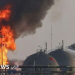 ألسنة لهب ودخان تتصاعد من منشأة نفطية تابعة لأرامكو السعودية بعد هجوم، مع سماء داكنة في الخلفية.