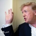 صورة للرئيس الأمريكي دونالد ترامب يتحدث في مؤتمر صحفي مع خلفية علم الولايات المتحدة