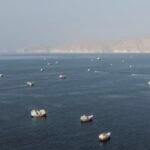 صورة جوية لمضيق هرمز تظهر سفناً تجارية، مع إشارة إلى التوترات الجيوسياسية بين إيران والولايات المتحدة.