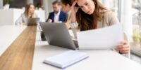 An overwhelmed employee juggling multiple tasks at a desk, symbolizing the 'two-job job' phenomenon.