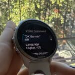 A close-up of a Garmin smartwatch screen displaying battery life, with an overlay indicating the 'OK Garmin' voice assistant feature.