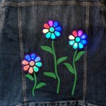 A denim jacket adorned with glowing, 3D-printed LED flowers, showcasing a modern twist on classic bedazzling.