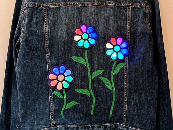 A denim jacket adorned with glowing, 3D-printed LED flowers, showcasing a modern twist on classic bedazzling.