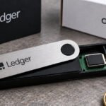 Illustration of a Ledger hardware wallet with a magnifying glass highlighting a suspicious implant, symbolizing a security breach.