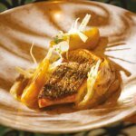 Un filet de bar mariné à l'unilatérale avec une peau croustillante, accompagné de fenouil fondant et nappé d'un beurre blanc citronné, décoré de pluches de fenouil frais et d'un filet d'huile d'olive.