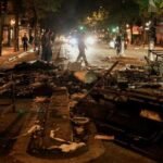 Vue aérienne d'une foule dense de manifestants défilant dans une rue urbaine, avec des drapeaux et des pancartes visibles, sous un ciel couvert, illustrant l'ampleur de la mobilisation du 17 octobre.