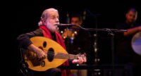 Marcel Khalifé jouant du luth sur scène, avec un éclairage artistique