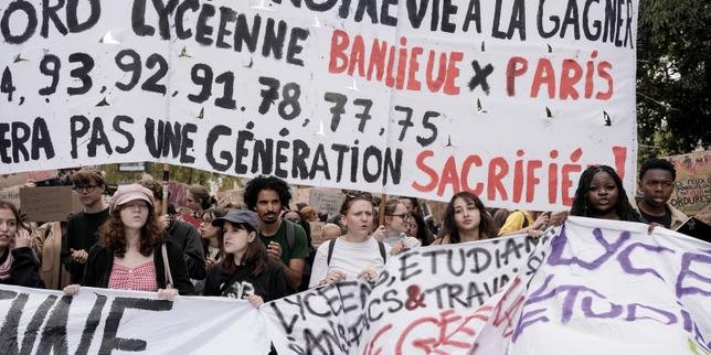 Jeune manifestant lycéen brandissant un drapeau français lors d'un défilé, avec d'autres élèves en arrière-plan et des fumigènes