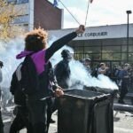Un groupe de lycéens manifestant, pancartes à la main, face à des forces de l'ordre, symbolisant la tension du mouvement. L'image pourrait montrer des jeunes visages, certains masqués, dans une atmosphère de protestation urbaine.