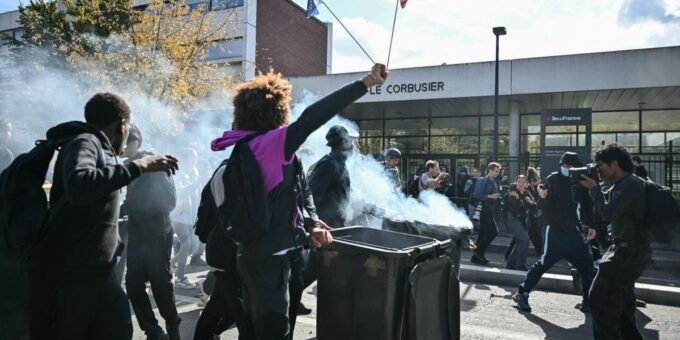 Un groupe de lycéens manifestant, pancartes à la main, face à des forces de l'ordre, symbolisant la tension du mouvement. L'image pourrait montrer des jeunes visages, certains masqués, dans une atmosphère de protestation urbaine.