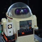 From 1984 to AI: How a Vintage Omnibot Robot Butler Got Its Modern Brain 6 A vintage Tomy Omnibot robot with a modern 3D-printed AI companion, Ring-O, on its arm, looking at a laptop.