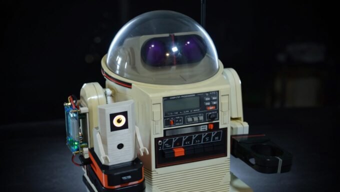 A vintage Tomy Omnibot robot with a modern 3D-printed AI companion, Ring-O, on its arm, looking at a laptop.