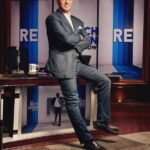 Rich Eisen smiling in a broadcast studio, surrounded by sports media equipment
