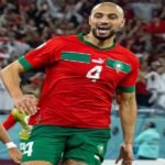 Sofyan Amrabat souriant, portant un maillot de football, lors d'une conférence de presse ou d'une séance photo officielle.