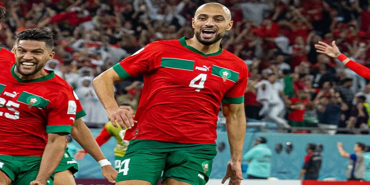 Sofyan Amrabat souriant, portant un maillot de football, lors d'une conférence de presse ou d'une séance photo officielle.