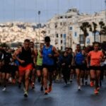 Des coureurs s'élançant sur la ligne de départ du Marathon de Tanger, avec la mer Méditerranée en arrière-plan et l'ambiance festive de l'événement.
