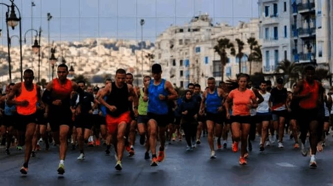 Des coureurs s'élançant sur la ligne de départ du Marathon de Tanger, avec la mer Méditerranée en arrière-plan et l'ambiance festive de l'événement.