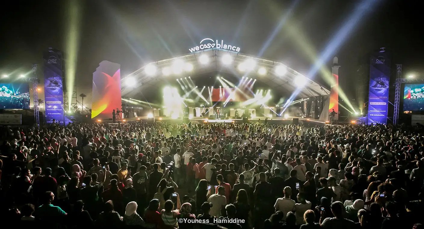 Scène de concert en plein air sur la Place Rachidi à Casablanca, avec des artistes en performance et une foule enthousiaste célébrant la Fête de l'Unité.