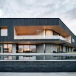 A boomerang-shaped modern home by CLB Architects cantilevered over a rugged Wyoming landscape, featuring a shadowed wood exterior blending with nature.