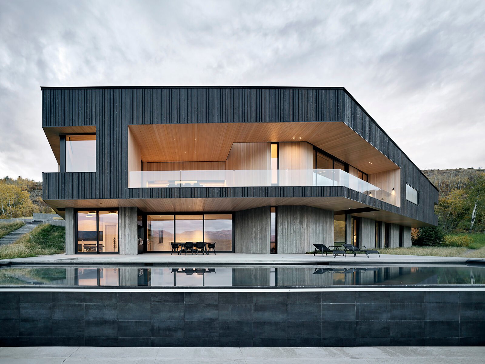A boomerang-shaped modern home by CLB Architects cantilevered over a rugged Wyoming landscape, featuring a shadowed wood exterior blending with nature.